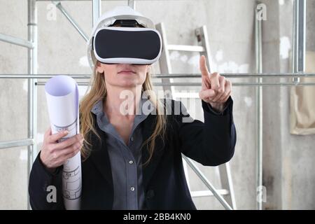 woman architect or construction engineer wear virtual reality glasses and helmet and touch screen inside a building site with ladder and scaffolding i Stock Photo