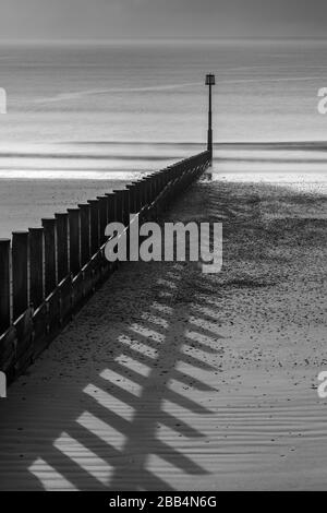 Shadows raking across the sand from timber groynes on Dawlish Warren beach Stock Photo