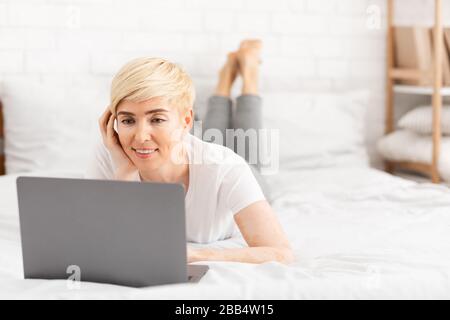 Happy mature woman laying in bed and watching movie Stock Photo