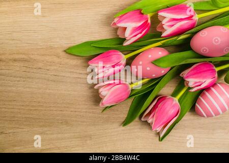 A bunch of fresh pink and white tulip flowers with green leaves and Easter eggs placed on wooden table, copy space, top view, spring flat layout decor. Stock Photo