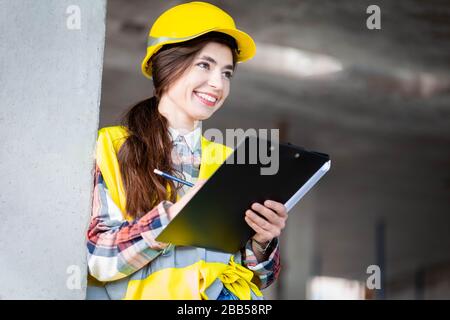 Woman in a protective helmet and a reflective vest conducts an inspection at a construction site Stock Photo