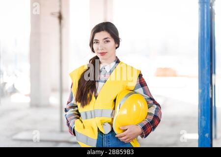 Female engineer stands at a construction site and holding a hardhat in hand Stock Photo