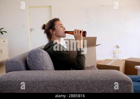 Woman in Social Distancing drinking a beer in her sofa Stock Photo