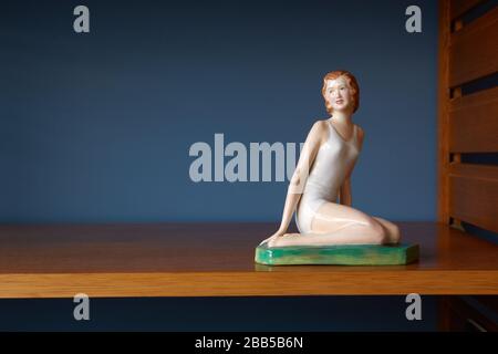 Photograph of a porcelain figurine of kneeling woman on a shelf. Stock Photo