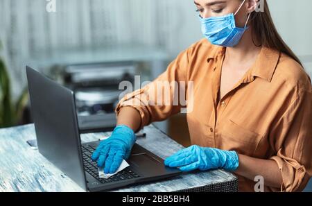 Woman in quarantine wearing gloves cleaning laptop keyboard Stock Photo