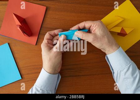 A photograph, from above, of a man's hands showing the process of making an Origami swan. Stock Photo