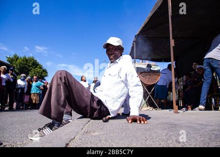 Cape Town, South Africa. 30th Mar, 2020. an elderly man sits on the pavement outside a shopping centre in Philippi to collect his social grant payment after the South African government declared a 21 day COVID-19 lockdown as part of the State of National Disaster declaration by President Cyril Ramaphosa. The Health Ministry has asked residents to observe the regulations, practise hygiene, stay at home and practise social distancing. Credit: Roger Sedres/Alamy Live News Stock Photo