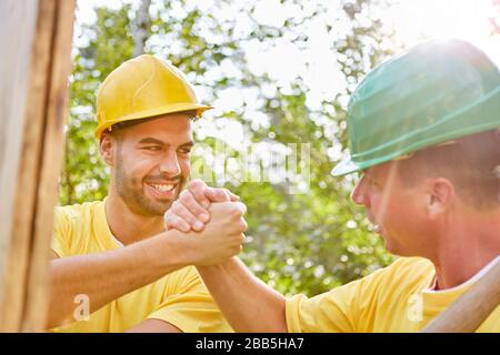 Happy artisans do teamwork on house building and hold hands Stock Photo