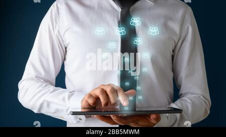 Front view of a businessman using digital tablet with many glowing people icons coming out of it. Conceptual of social distancing and social media int Stock Photo