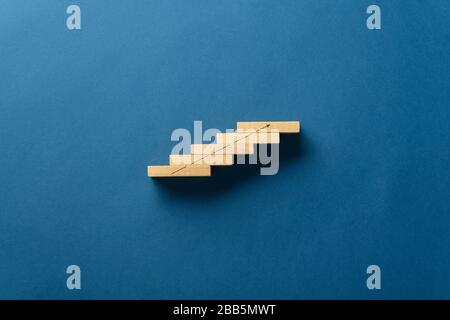 Wooden pegs placed in a stairway like structure with a rising arrow drawn on it. Over blue background with plenty of copy space. Stock Photo