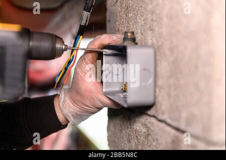 Male electrician pre drilling hole for socket to be fixed onto wall Stock Photo