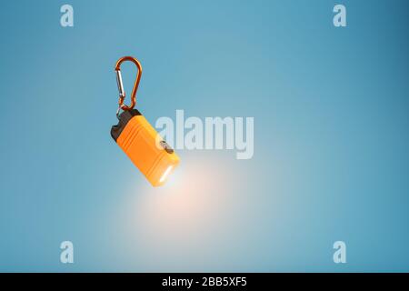 Orange led Flashlight with a carabiner on a blue background. LED lights in flight. Stock Photo