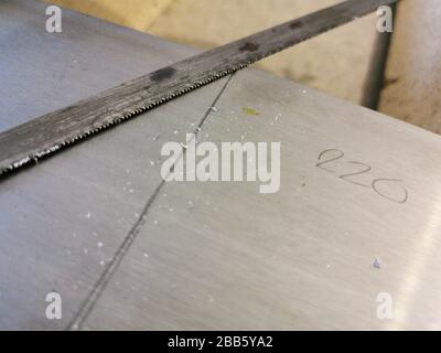 Rusty old hand saw blade cutting through aluminum plate during furniture restoration process at home with measurement value and pencil markings Stock Photo