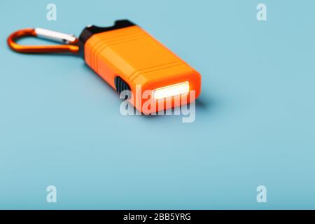 Orange led Flashlight with a carabiner on a blue background. LED lights in flight. Stock Photo