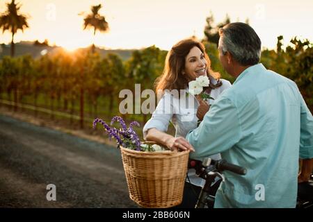 Happy mature couple putting flowers in basket of their bicycle. Stock Photo