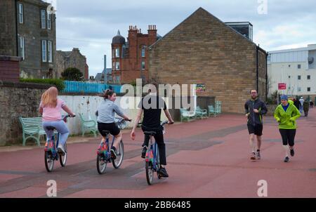 Portobello, Edinburgh, cycling Scotland, UK. 30th Mar 2020. Cyclists on council hire bikes and joggers on the promenade not really giving physical social distance from one another. Stock Photo