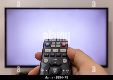 Person pointing a TV remote and pressing buttons in front of a TV with blank screen Stock Photo