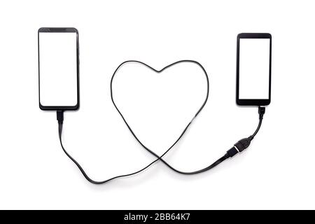 Hand connecting two smartphones with a heart shaped USB cable. Long distance relationship concept. Stock Photo