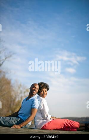Happy couple sitting on wharf together. Stock Photo