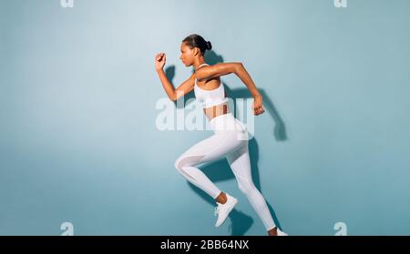 Side view of young woman running. Fitness model exercising against blue background. Stock Photo