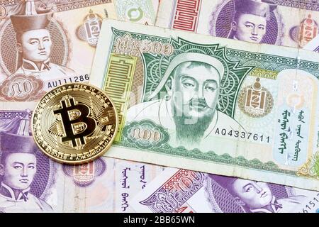 Close-up on a golden Bitcoin coin on top of a stack of Mongolian Tögrög banknotes. Stock Photo