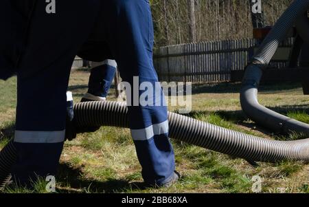 Man worker holding pipe, providing sewer cleaning service outdoor. Sewage pumping machine is unclogging blocked manhole Stock Photo