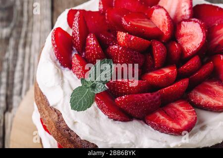 Homemade sponge cake with strawberries and cream on rustic wooden table close up, summer dessert Stock Photo