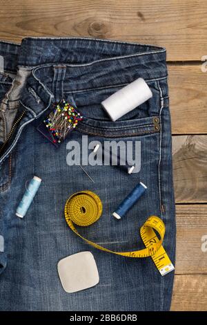 Blue denim cotton fabric trousers with tailor's tools on brown wood background - jeans fashion mending or repair concept, flat lay top view from above Stock Photo