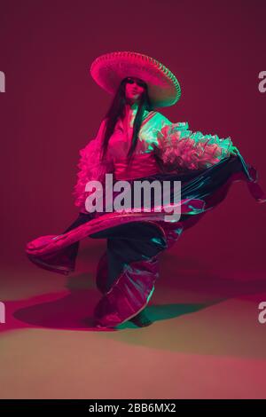 Fabulous Cinco de Mayo female dancer on purple studio background in neon light. Beautiful female model in traditional costume and sombrero dancing. Celebration, holiday, beauty and fashion concept. Stock Photo