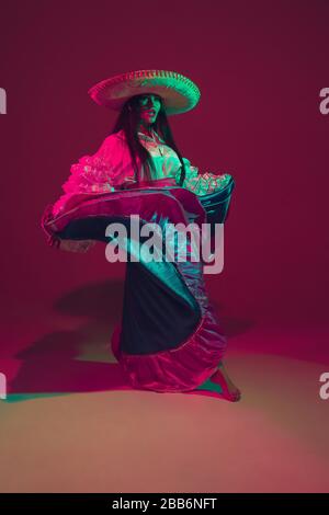 Fabulous Cinco de Mayo female dancer on purple studio background in neon light. Beautiful female model in traditional costume and sombrero dancing. Celebration, holiday, beauty and fashion concept. Stock Photo