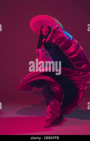 Fabulous Cinco de Mayo female dancer on purple studio background in neon light. Beautiful female model in traditional costume and sombrero dancing. Celebration, holiday, beauty and fashion concept. Stock Photo
