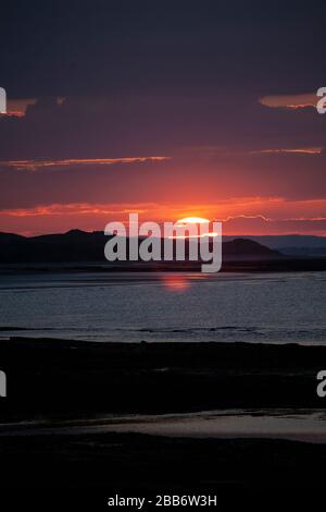 A deep red sunset sky as the sun sinks over the Northumberland coast in Northern England, viewed from the village of Seahouses on a summer evening. Stock Photo