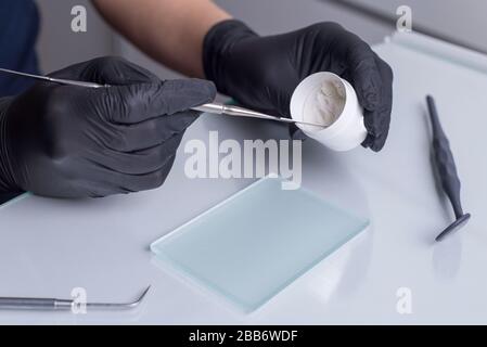 closeup, top view of the dentists hands, in gloves, holding a preparation preparation tool in his hand. Against the background of other dental instrum Stock Photo