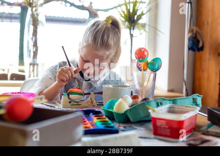 Portrait of adorable blonde girl at home painting easter eggs Stock Photo