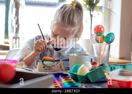 Portrait of adorable blonde girl at home painting easter eggs Stock Photo