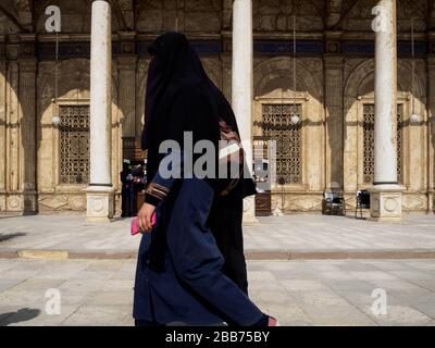 Cairo, Egypt, February, 2020, a traditional dressed egyptian woman passing by a mosque in cairo Stock Photo