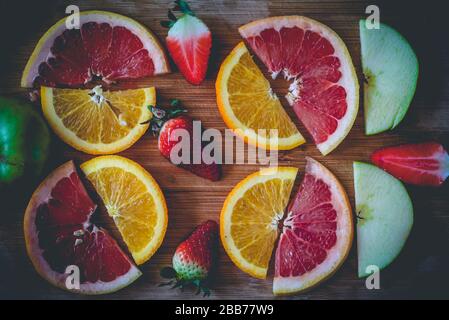 Flat lay image of cut ruby red grapefruit, orange, strawberries and green apple aranged on kitchen cutting board Stock Photo