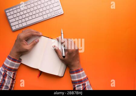 overhead view of hands holding a blank book ready on orange background  Stock Photo