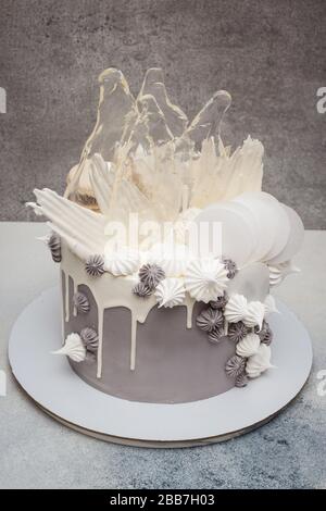 Elegant grey cake with modern design. Caramel, waffle paper, french meringues and white chocolate decoration. Grey background. Stock Photo