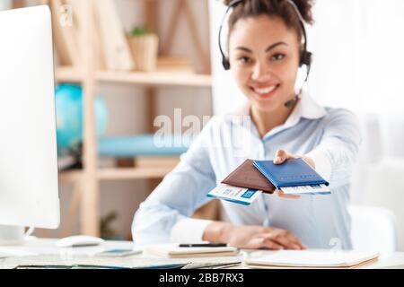 Tour agent in headset sitting at table in office giving passports and tickets blurred smiling happy Stock Photo