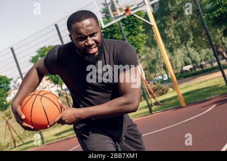 Outdoors Activity. African man running with ball on court motivated Stock Photo