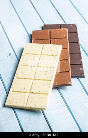 White, milk and dark chocolate bars on blue wooden table. Stock Photo