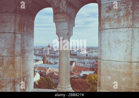Cityscape of Budapest, Hungary photographed through the arch window of the Fishermans Bastion. Hungarian Parliament Building, Orszaghaz, in the far background on the other side of the Danube river. Stock Photo