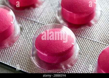Pills in blister. Macro close up of red medical pills in blister pack strip on a grey background for use as a medical or pharmaceutical background. Stock Photo