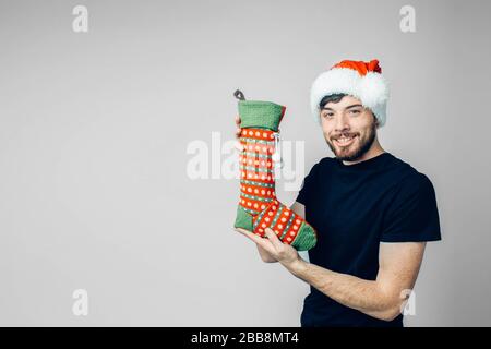 Young bearded man isolated over background. Cheerful positive male person hold festive sock for presents and gifts. Stand alone and posing. New year m Stock Photo