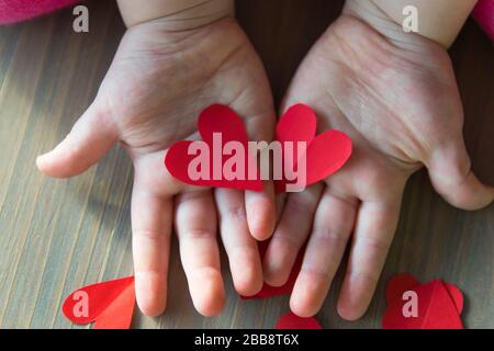 Two red hearts from paper in childshands on the wood background. Sign of love. A gift for Valentines Day and Mothers Day. Stock Photo