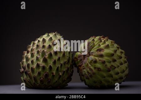 Still life of Soursop or Graviola fruit with prickly vibrant green peel against a dark gray background on a grey surface. Low key studio shot of fresh Stock Photo