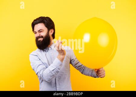 Man holding needle over yellow air balloon, a moment before bubble burst. Stock Photo