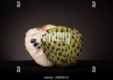Funny frame of two halves of Soursop or Graviola fruit with white pulp and black hard seeds and other half showing its prickly vibrant green peel Stock Photo