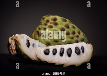 Close up of slices of Soursop or Graviola fruit with black seeds and white pulp showing and prickly vibrant green peel of other half behind Stock Photo